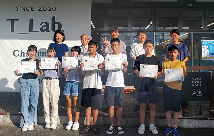 Children holding certificates in the front row, adults standing in the back row for a photo.